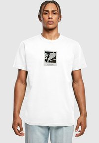 Hvid bomulds T-shirt med et grafisk tryk i en sort ramme. Designet inkluderer abstrakte former og ordet "glamorøs" nederst.