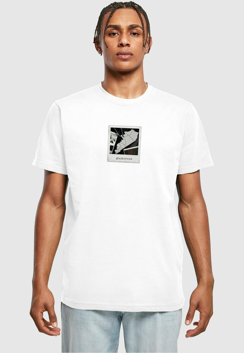 Hvid bomulds T-shirt med et grafisk tryk i en sort ramme. Designet inkluderer abstrakte former og ordet "glamorøs" nederst.