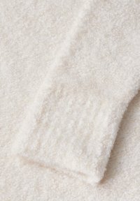 Tessuto bianco e morbido con una superficie testurizzata. Presenta un polsino a coste e un aspetto leggero e peloso. Ideale per calore e comfort.