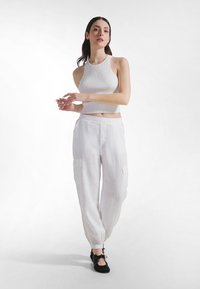 Biały prążkowany krótki top zestawiony z lekkimi, luźnymi białymi spodniami cargo z bocznymi kieszeniami i elastycznymi mankietami. Czarne buty dopełniają stylizację.