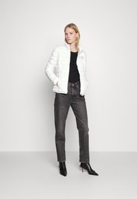 Hvit, quiltet boblejakke med ståkrage og glidelås. Svart T-skjorte under, kombinert med høyhulls mørke jeans og spisse hæler.