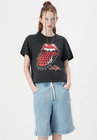 Black graphic t-shirt with a red mouth design, paired with light denim shorts featuring side stripes and an elastic waistband.