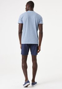 Camiseta a rayas azul claro con mangas cortas, combinada con pantalones cortos azul marino. El modelo lleva zapatos casuales azules. Tela suave con textura mínima.