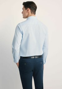 Jasnoniebieska koszula w kratę z długimi rękawami, kołnierzykiem zapinanym na guziki i gładką teksturą, noszona z granatowymi spodniami i czarnym paskiem.