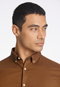 Camicia marrone con colletto a ripiegare, caratterizzata da bottoni bianchi e una sottile trama, vestibilità su misura che enfatizza linee pulite.