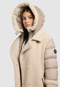 Beige puffer winterjack met een dubbelzijdig ontwerp, fleece textuur, grote capuchon en logo accent op de mouw. Ritszakken aan de voorkant.