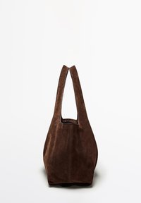 Brown suede tote bag with a unique cutout handle design. Soft texture, slouchy shape, and minimal stitching detail on the sides.