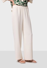 Crème-kleurige wijdvallende broek met een elastische tailleband, gemaakt van een zachte, gladde stof, gecombineerd met beige platte sandalen.