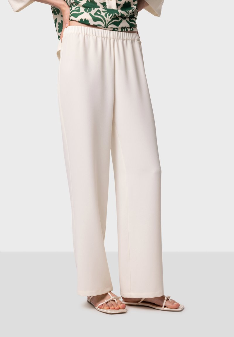 Crème-kleurige wijdvallende broek met een elastische tailleband, gemaakt van een zachte, gladde stof, gecombineerd met beige platte sandalen.