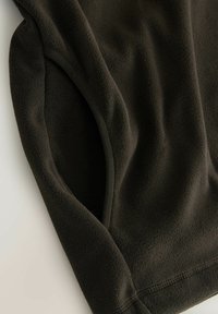 Sötétbarna polár pulóver sima, puha anyaggal. Ívelt, varrott szegéllyel és bevarrt ujjakkal rendelkezik, kényelmes szabással.