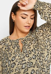 Blusa in stampa leopardata in tessuto leggero e semitrasparente; presenta un colletto con fiocco, dettagli a bottoni sulla parte anteriore e maniche a sbuffo con polsini arricciati.