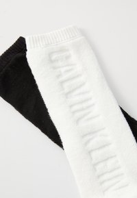 Meias em mistura de algodão com uma seção preta e uma seção branca com o logo "CALVIN KLEIN" em relevo, punho canelado e textura suave.
