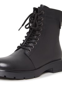 Bottine noire en cuir avec semelle épaisse et fermeture à lacets à l'avant avec œillets métalliques sur fond blanc.