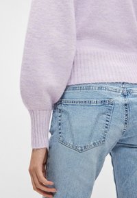 Υφασμάτινο πουλόβερ λεβάντας με φουσκωτά μανίκια και ριμπ μανσέτες, σε συνδυασμό με ανοιχτόχρωμο τζιν τζιν με δύο πίσω τσέπες.