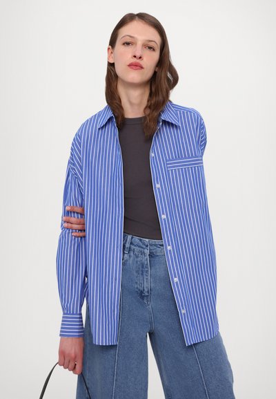 Blue and white striped shirt with a collared neckline, button-down front, and single chest pocket, paired with high-waisted denim trousers.
