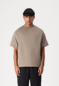 T-shirt in cotone grigio con scollatura a girocollo, maniche corte, presenta un piccolo logo arancione sul lato sinistro, vestibilità rilassata.