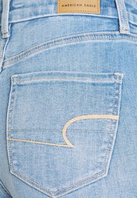 Ljust blå denimjeans med en bakficka som har en gyllene broderidetalj. Tyget har en mjuk textur och en något bleknad finish.