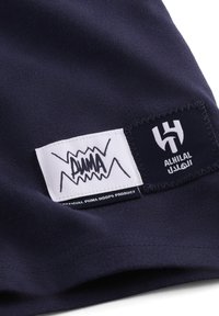 Marineblåt bomuldsstof med to labels: en med et hvidt "PUMA" logo og den anden med "AL HILAL," kantet med kontraststing.