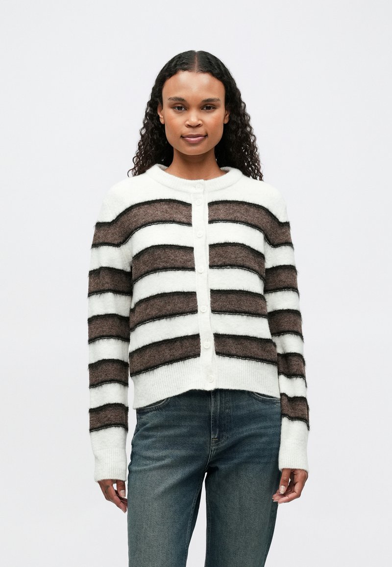 Cardigan a righe bianco, marrone e nero. Texture morbida, scollatura rotonda, chiusura con bottoni e polsini a costine. Indossato con jeans.