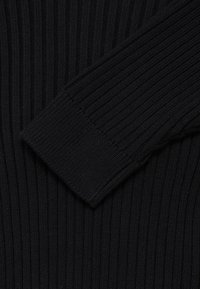 Gros plan sur un tissu tricoté côtelé noir mettant en évidence une manche pliée avec une couture serrée au niveau du poignet.