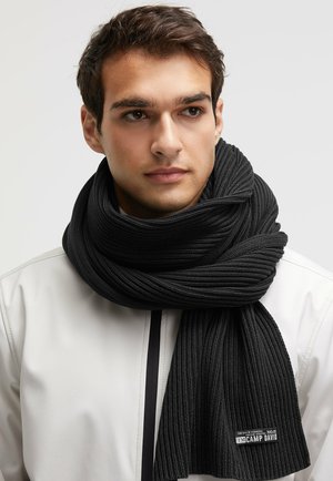 Black ribbed knit scarf with a woven texture, draped around the neck, featuring a branded tag with "CAMP DAVID" on the end.