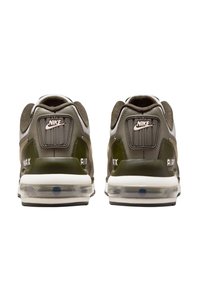 Zapatillas Nike Air Max con parte superior gris, acentos en verde oscuro y amortiguación de aire visible en el talón. Presenta el logo de la marca en la lengüeta del talón.