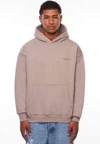 Beige hoodie gemaakt van zachte stof, met een voorzak, ribgebreide boorden en een klein reliëflogo op de borst.