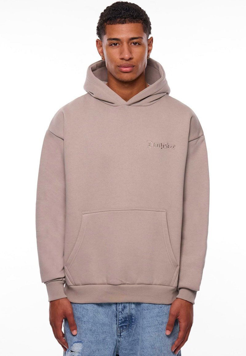 Beige hoodie gemaakt van zachte stof, met een voorzak, ribgebreide boorden en een klein reliëflogo op de borst.