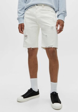 White denim shorts with frayed hems and multiple distressing details. Worn with black sneakers and white crew socks.