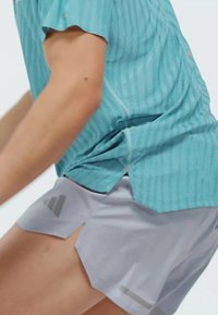 Camiseta atlética azul clara con rayas verticales y mangas cortas, combinada con pantalones cortos grises con aberturas laterales en ángulo y un logo en el dobladillo.