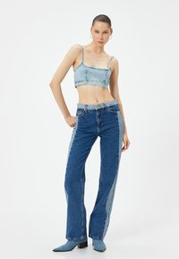 Top corto in denim e jeans a vita alta in diverse tonalità di blu. I jeans presentano un design di color blocking unico lungo i fianchi.