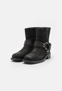 Bottines en daim noir avec une large sangle et un détail de boucle en argent. Semelle plate, bout rond et texture lisse. Design classique et minimal.