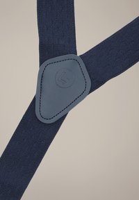 Granatowe szelki z tkaniny z teksturowanymi paskami i trójkątną skórzaną łatą z logo. Regulowane elementy z metalu.