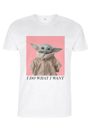 Weißes T-Shirt mit einem grafischen Motiv eines Charakters in einer beigen Jacke mit hohem Kragen, vor einem rosa Hintergrund, mit Text darunter.