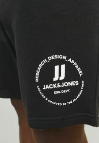 Pantaloni corti neri in cotone con un logo bianco circolare con il testo: "JACK & JONES" e "RESEARCH_DESIGN_APPAREL" sulla coscia sinistra.