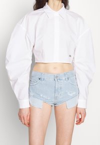 Wit cropped shirt met een knoopsluiting aan de voorkant en poffende mouwen, gecombineerd met lichtblauwe versleten denim shorts met een scalloped zoom.