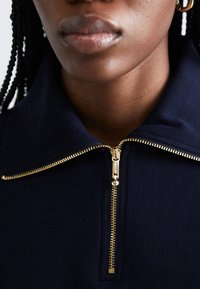 Maglione blu navy con zip dorata, dotato di collo alto e texture a costine. La zip è centrata e si estende fino al collo.