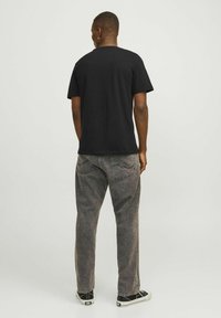 Camiseta de algodón negra de manga corta, acompañada de pantalones de mezclilla grises. El calzado presenta unas zapatillas de tela en blanco y negro.