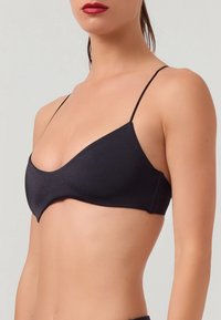 Svart bralette med tunna justerbara remmar, slät tyg, vågformad design och en minimalistisk silhuett utan synlig hårdvara.