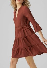 Vestido de color óxido en capas con mangas de campana tres cuartos, hecho de una tela texturizada, con un escote en pico y una silueta fluida.