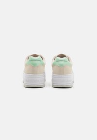 Sneaker beige con un accento verde menta sul tallone, materiale scamosciato testurizzato e una suola piatta bianca con marchio embossato.