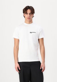 Weißes Baumwoll-T-Shirt mit Rundhalsausschnitt und kurzen Ärmeln. Schwarzes "KARL LAGERFELD JEANS"-Logo auf der oberen linken Seite.