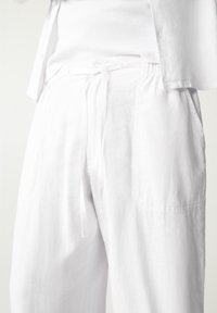 Hvide hørbukser med elastisk taljebånd og snøre, to sidelommer og en afslappet pasform. Stoffet har en glat tekstur.