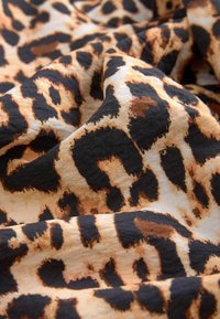 Leopardmønstret stof med en tekstureret overflade og intrikate pletter i sort, brunt og creme, der viser en tydelig variation i mønstret.