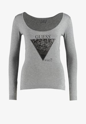 Szary długi rękaw, bluzka z okrągłym dekoltem, z czarnym graficznym wzorem w kształcie trójkąta, zawierającym tekst; połączona z czarnymi obcisłymi dżinsami i botkami do kostek.