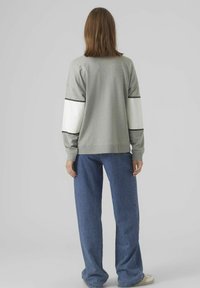 Grijze sweatshirt met witte mouwen, zwarte strepen en ribgebreide manchetten. Gecombineerd met wijdvallende blauwe jeans, met een lage taille en lichte slijtage.