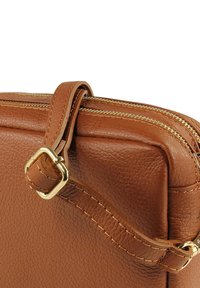 Braune Tasche aus Kunstleder mit strukturierter Oberfläche, zwei goldfarbenen Reißverschlüssen und einem Riemen mit einer Schnalle aus goldfarbenem Metall.