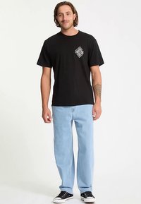 Zwart katoenen T-shirt met een afbeelding aan de voorkant, gecombineerd met lichtblauwe spijkerbroek en zwarte sneakers. Casual pasvorm, korte mouwen, rechte pijpen.