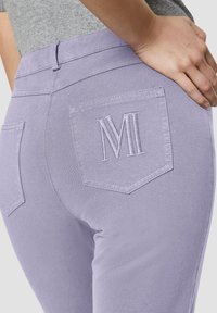 Aansluitende lavendel jeans met een gladde textuur, voorzien van twee achterzakken, waarvan er één geborduurd is met de letter 'M' in bijpassende draad.