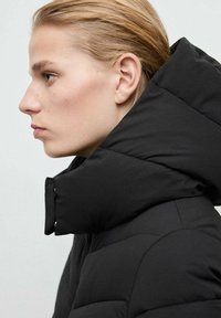 Czarna ocieplana kurtka puchowa z wysokim kołnierzem i pikowanym wzorem. Gładka faktura i wyraźna sylwetka podkreślają ciepło i styl.